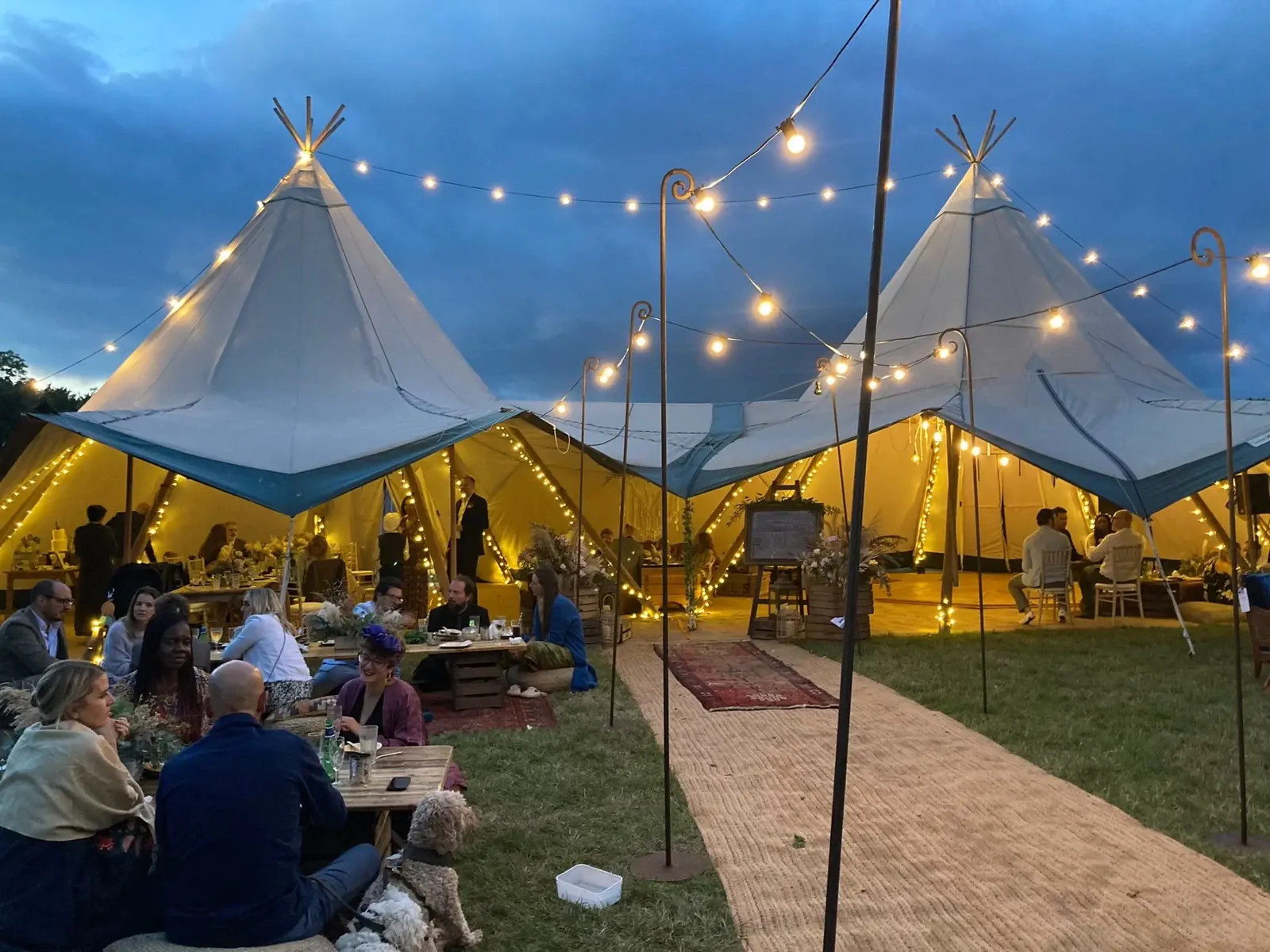 Wedding guests dining outside lit tipis at dusk, catered by Fan Thai Sticks